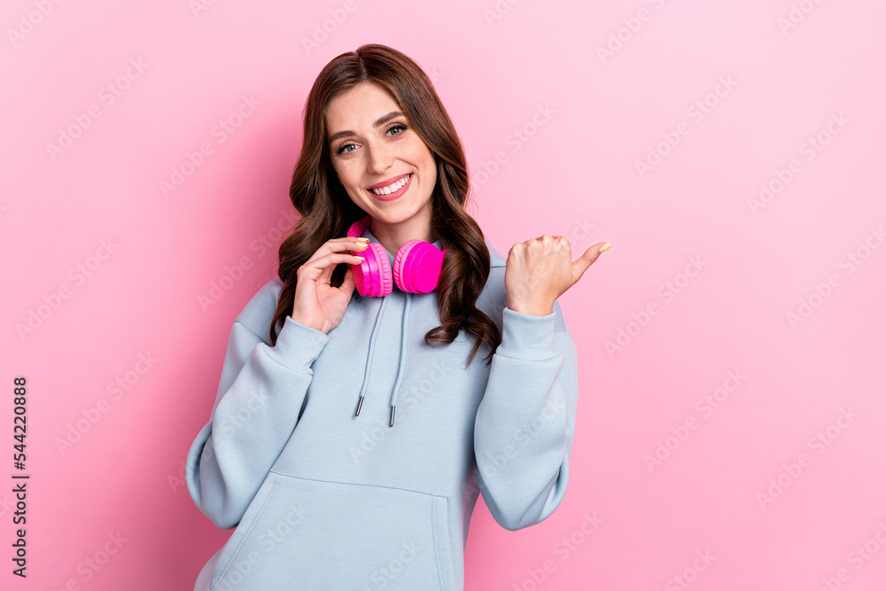 Portrait of cheerful pretty girl hand touch headphones indicate thumb finger empty space isolated on pink color background Portrait of cheerful pretty girl hand touch headphones indicate thumb finger empty space isolated on pink color background