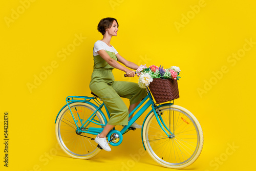 Full size photo of lovely young woman driving florist flower delivery bike dressed stylish khaki outfit isolated on yellow color background © deagreez