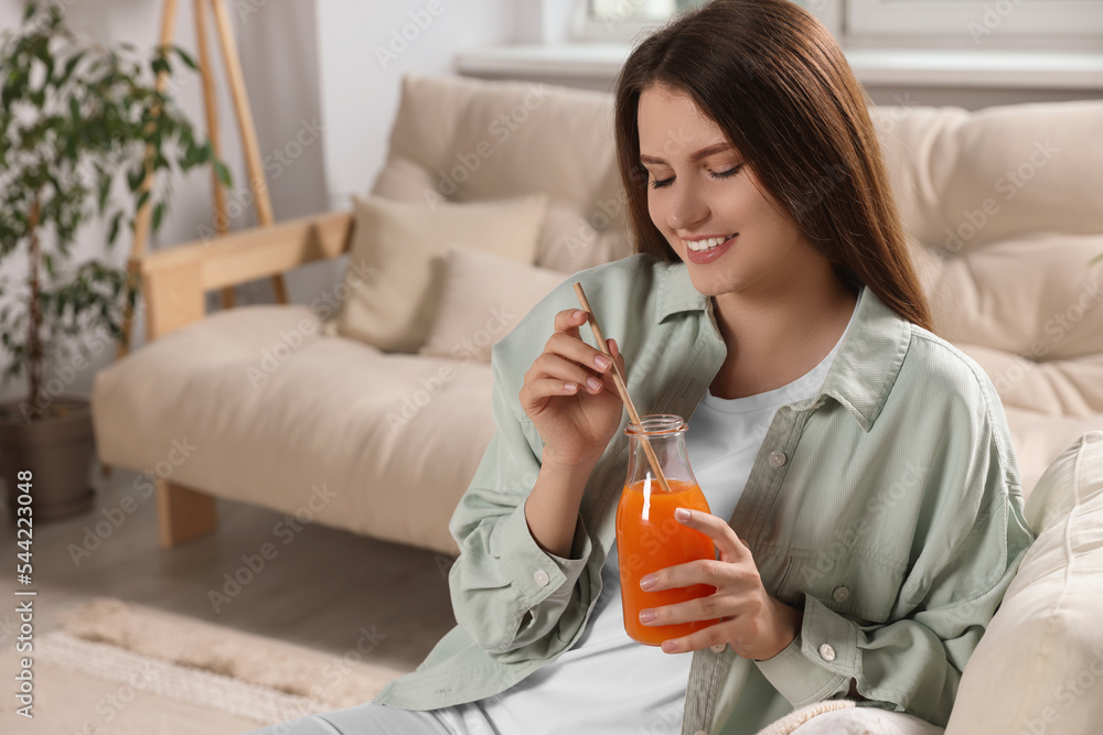 Beautiful young woman with glass bottle of juice on sofa at home Beautiful young woman with glass bottle of juice on sofa at home