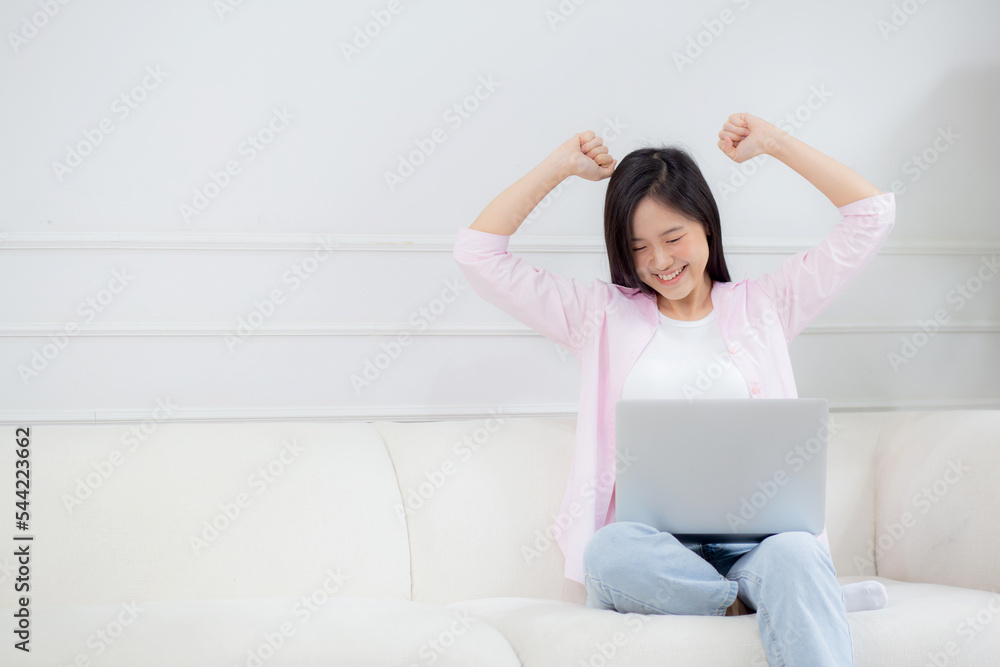 Happiness young asian woman sitting on sofa and working on laptop computer while successful and excitement at home, freelance female using notebook and achievement, business and lifestyles concept. Happiness young asian woman sitting on sofa and working on laptop computer while successful and excitement at home, freelance female using notebook and achievement, business and lifestyles concept.