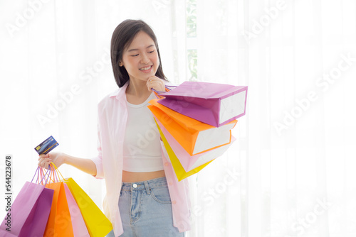 Young asian woman standing holding credit card and paper bag with satisfied, happy female carrying paper bag and debit card paying with transaction financial, purchase and payment, business concept.