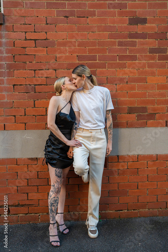 cool lesbian couple kissing against orange brick wall in street © Andy Connell