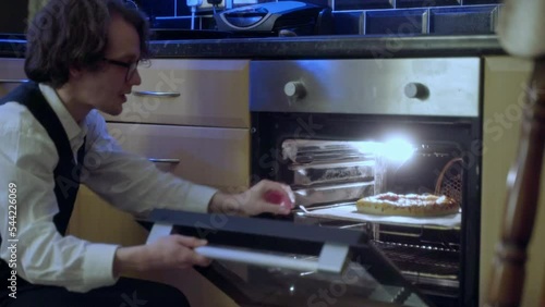 A young man has his pizza in the oven and prepares for a meal photo