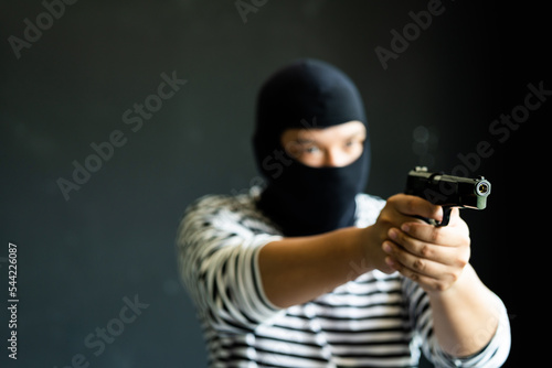 Masked robber with gun. Concept of crime and fire arm assault with mature man. Armed robbery on black. 