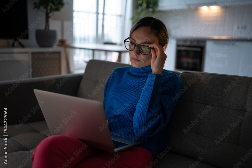 Pensive businesswoman in glasses looking at laptop screen sit on couch. Thoughtful young woman work on difficult research project, reading email, pondering strategy, watch online educational webinar. Pensive businesswoman in glasses looking at laptop screen sit on couch. Thoughtful young woman work on difficult research project, reading email, pondering strategy, watch online educational webinar.