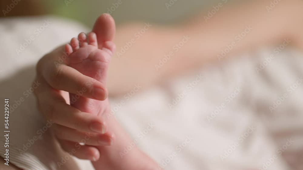 A woman's hand gently touches the legs of a newborn baby taken close-up. A woman's hand gently touches the legs of a newborn baby taken close-up.