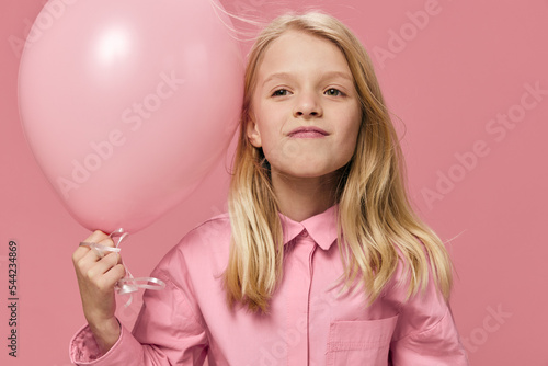 joyful school-age girl stands on a pink background with a big balloon in her hand and smiles broadly while looking at the camera. Horizontal photo with blank space for advertising layout insert