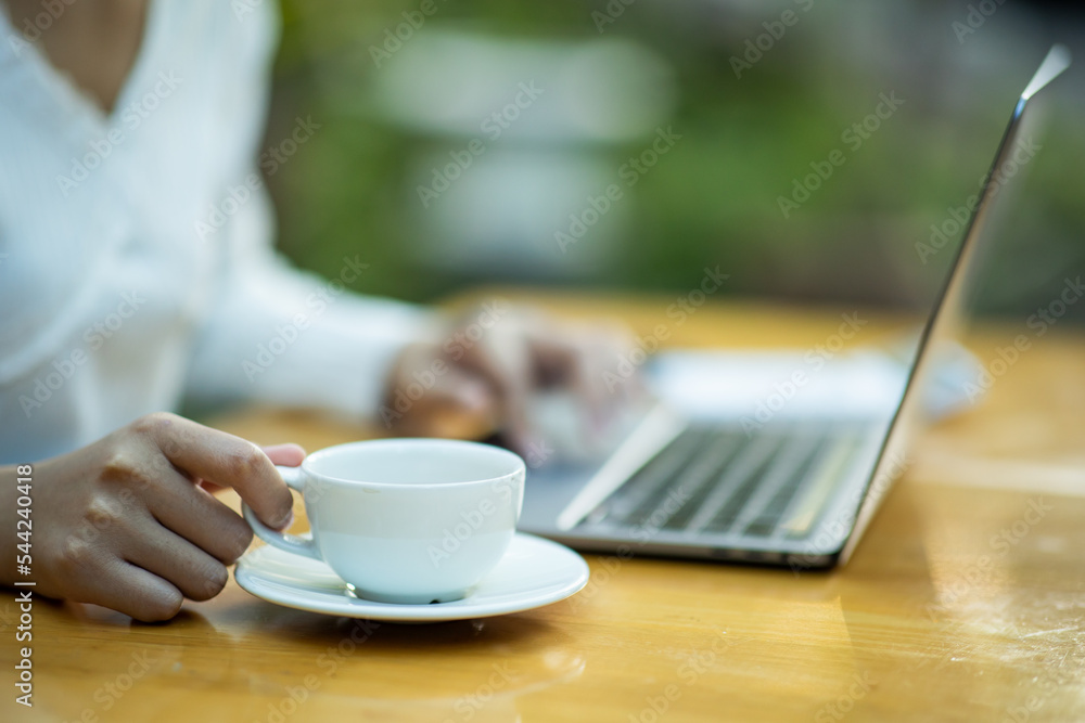 Young woman sitting in a coffee shop at a wooden table Drink coffee and use a laptop young women surfing the internet chat blogging woman holding a cup of coffee in a cafe. Young woman sitting in a coffee shop at a wooden table Drink coffee and use a laptop young women surfing the internet chat blogging woman holding a cup of coffee in a cafe.