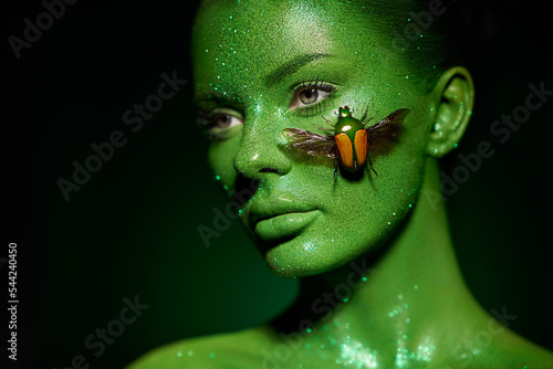 Fotografia Fashion model woman skin face in bright sparkles with green beetle colorful neon lights, beautiful girl sexy lips