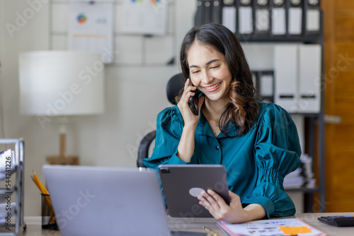 Corporate Communication. Asian Businesswoman Talking On Mobile Phone Working On Laptop In Modern Office. Free Space