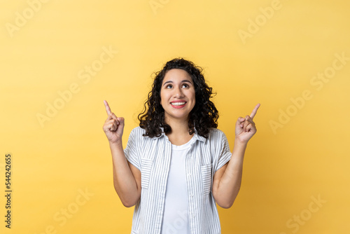 Fotografia, Obraz Portrait of satisfied delighted woman with dark wavy hair pointing up at empty place for ad content and expressing positive emotions