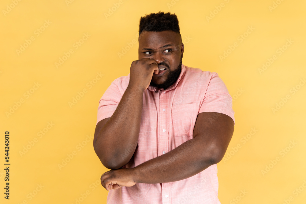 Anxiety disorder. Portrait of stressed out worried man in pink shirt biting nails, nervous about troubles, panicking and looking scared, looking away. Indoor studio shot isolated on yellow background. Anxiety disorder. Portrait of stressed out worried man in pink shirt biting nails, nervous about troubles, panicking and looking scared, looking away. Indoor studio shot isolated on yellow background.