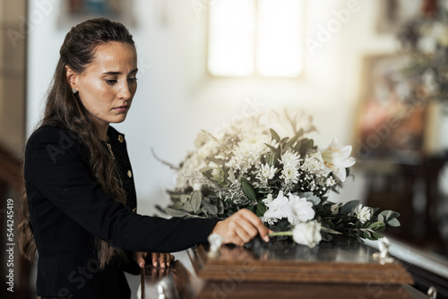 Funeral, sad and woman with flower on coffin after loss of a loved one, family or friend. Grief, death and young female putting a rose on casket in church with sadness, depression and mourning