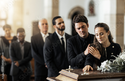 Death, funeral and family touching coffin in a church, sad and unhappy while gathering to say farewell. Church service casket and sad man and woman looking upset while greeting, goodbye and rip photo
