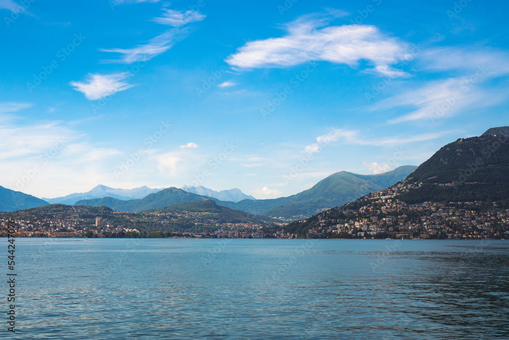 Beautiful panoramic view of Lake Lugano and the green Swiss Alps in the background on a sunny summer day. Canton of Ticino, Switzerland.