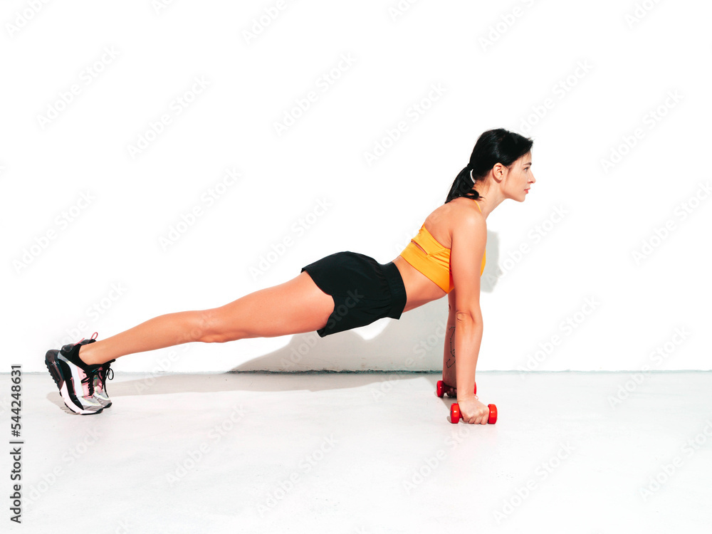 Fitness confident woman in black sports clothing. Sexy young beautiful model with perfect body. Female isolated on white wall in studio. Stretching out before training. Pushing up on dumbbells