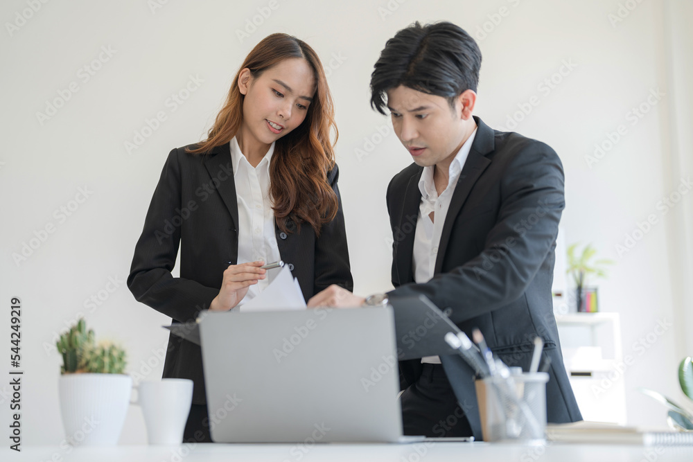 Business people stand together at a desk talking on their laptops Business people stand together at a desk talking on their laptops