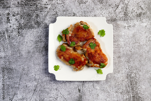 Crispy skin chicken Tapaka thighs with herbs on a white square  plate on a dark background. Top view, flat lay photo