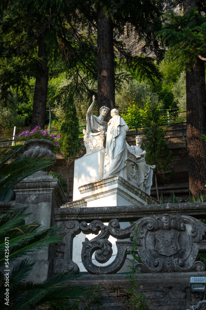 View to ancient sculptures by Giovan Battista Comolli in the botanical garden under the shade of cypress tree of the Villa Monastero in Varenna, on the shore of Lake Como, Province of Lecco, Italy.