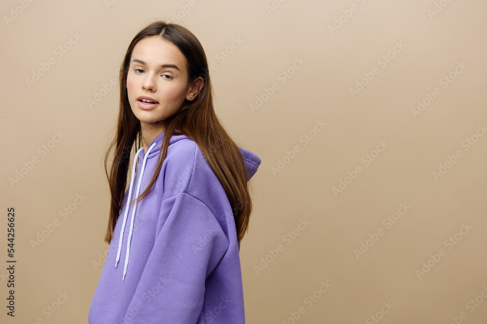 Fototapeta premium Horizontal photo of a pleasant, calm, relaxed woman standing sideways to the camera in a purple suit on a beige background