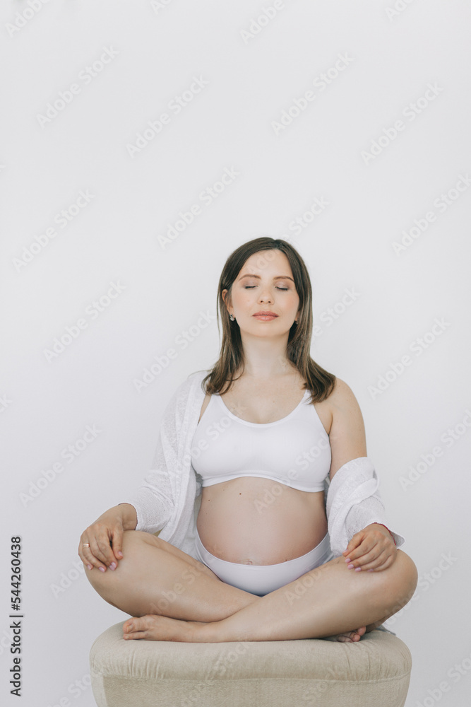A pregnant woman sits in a lotus position on a white background. The concept of conscious fatherhood, happy motherhood and easy pregnancy. A pregnant woman sits in a lotus position on a white background. The concept of conscious fatherhood, happy motherhood and easy pregnancy.
