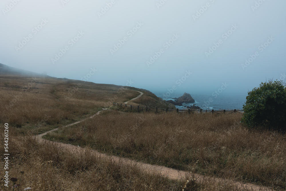 Obraz premium A path for walking along the blue ocean with a rocky shore in the fog. Picturesque weather and nature.