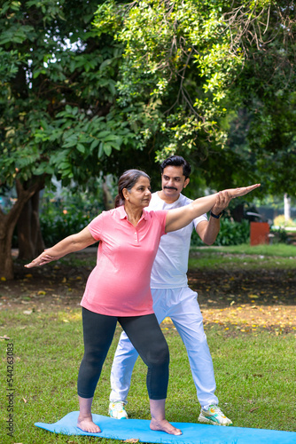 Indian male teacher or trainer teach yoga to young female student in the park. Sports and workout concept.