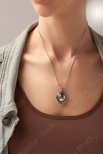 фотографія Cropped shot of a lady wearing a metal silver necklace made out of a chain with a dangling pendant with a red sparkling crystal