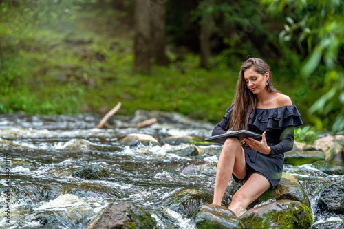 woman freelancer sitting on a rock in the river and using a laptop  travel or vacation work concept