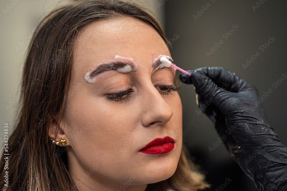an eyebrow artist is laminating the eyebrows of a beautiful client.