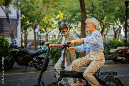 Cheerful seniors riding bicycle and scooter outside.