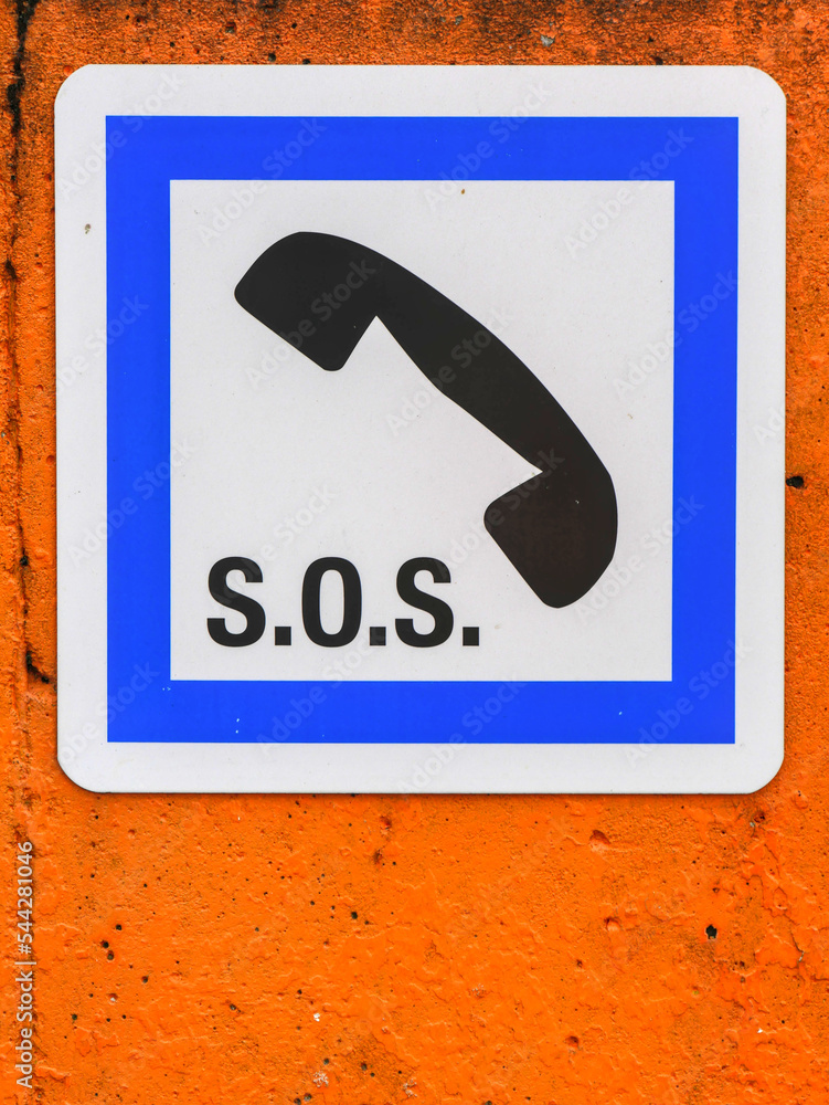 Obraz premium SOS sign composed of a telephone handset design and the SOS letters, in a blue square, on a old orange background.