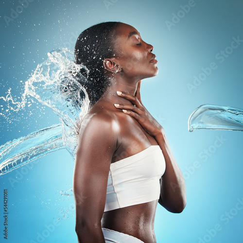 Water splash  black woman and shower for skincare  hygiene and cleaning body in blue mockup studio background. Bathroom  cleansing and attractive young female wet in the bathroom for skin hydration