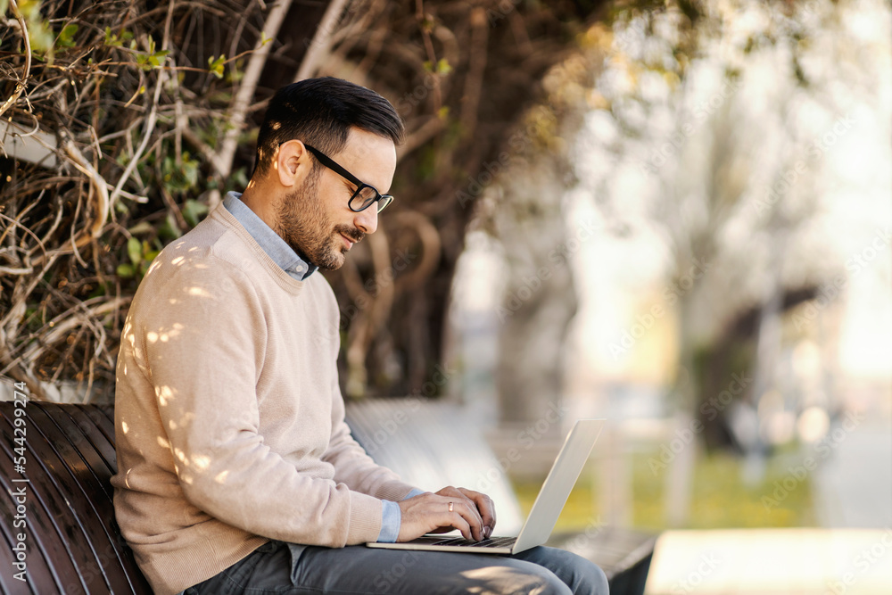A busy man in smart casual is sitting in park and typing on his laptop. Hands are on keyboard. A busy man in smart casual is sitting in park and typing on his laptop. Hands are on keyboard.