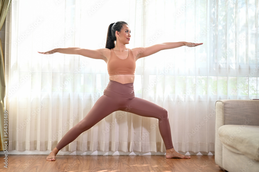 Sporty Asian woman practicing Warrior ii yoga pose, workout and cardio in her living room. Sporty Asian woman practicing Warrior ii yoga pose, workout and cardio in her living room.