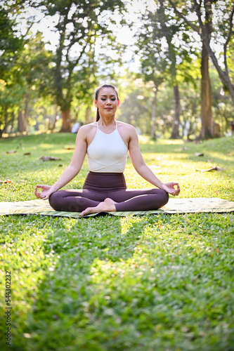Healthy Asian woman meditating, doing Lotus pose, practicing yoga in the park.
