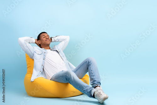 Studio portrait of relaxed cheerful man relaxing armchair isolated on blue wall