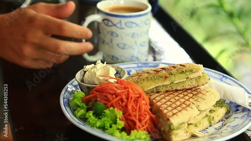 Selective focus on a plate of vegan panini for breakfast while a person drinks coffee in the background