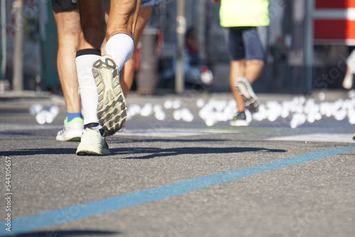 Foto dal basso di maratoneti che corrono, passando per un punto di ristoro con tanti bicchieri di plastica buttati a terra