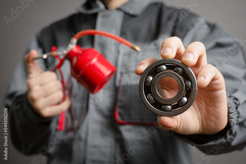 Car service worker holding in hands a red oil can and car parts on dark background closeup. © Dmitriy