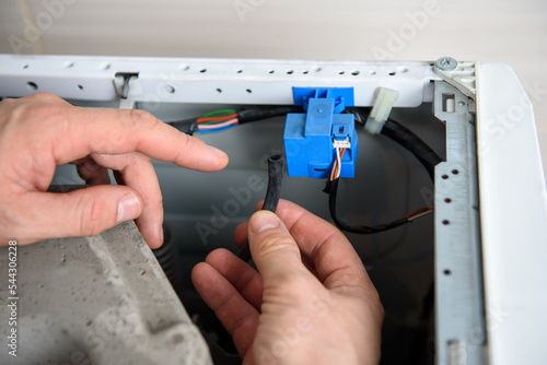 A man is fixing a washing machine. Repairman checks pressure switch