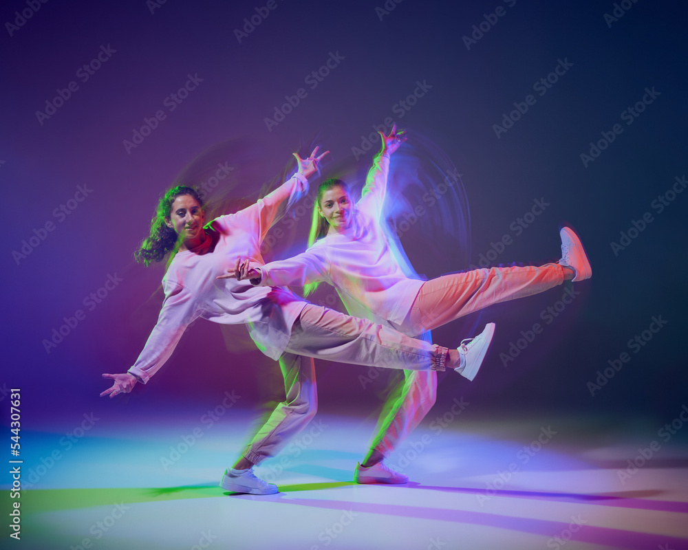 Portrait of young girls dancing hip-hop, contemp isolated over gradient blue purple background in neon with mixed light.