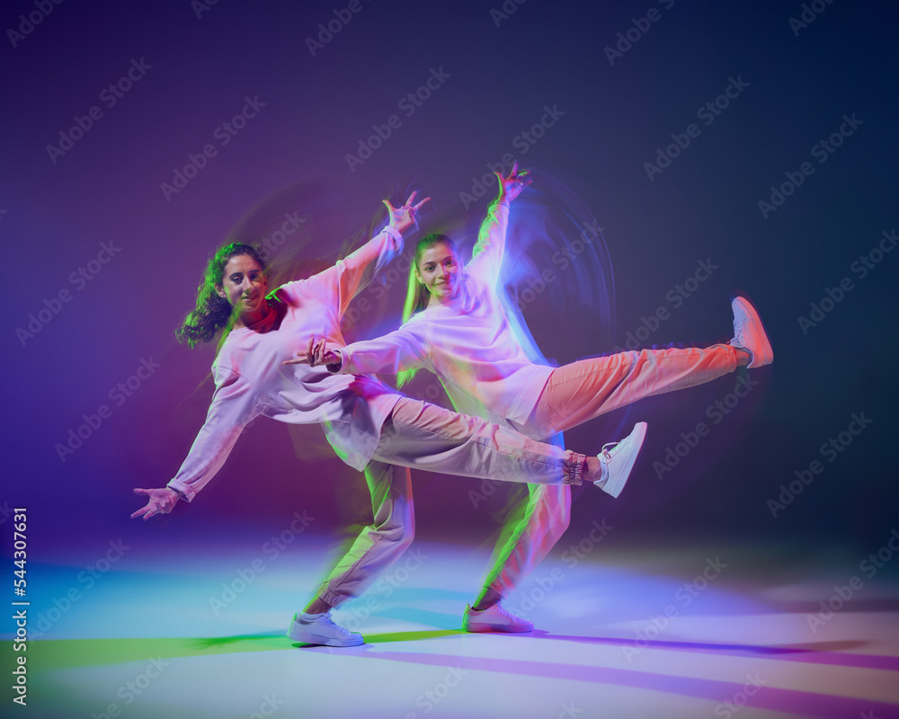 Obraz premium Portrait of young girls dancing hip-hop, contemp isolated over gradient blue purple background in neon with mixed light.