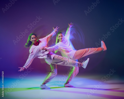 Portrait of young girls dancing hip-hop, contemp isolated over gradient blue purple background in neon with mixed light. © Lustre