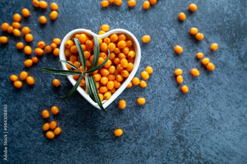 Sea buckthorn berries in a heart shaped bowl, orange healthy berries, macro. Rustic style, top view Sea buckthorn berries in a heart shaped bowl, orange healthy berries, macro. Rustic style, top view