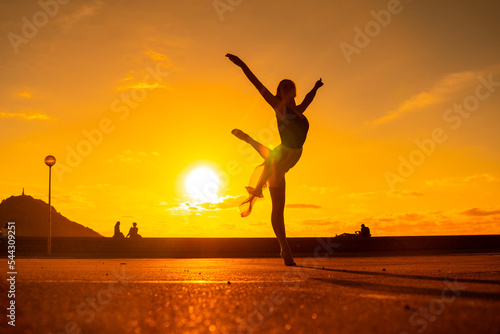 Silhouette of a young woman dancer by the beach at sunset raising her leg