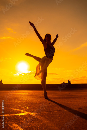 Silhouette of a young woman dancer by the beach at sunset doing an acrobatic