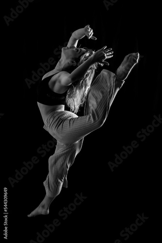 Young dancer in studio photo session with a black background, ballet, performing a jump in black and white