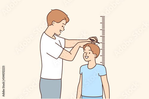 Smiling father measure son height near wall 