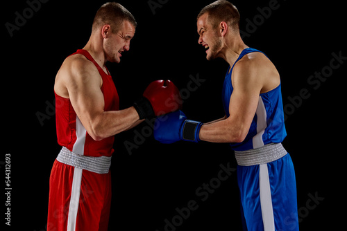 Greeting rival. Two twins brothers, professional boxers in blue and red sportswear boxing isolated on dark background. © master1305